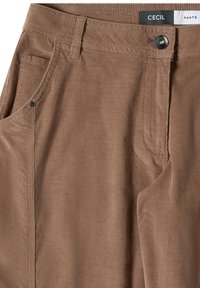 Pantalon en velours côtelé marron avec poches avant, passants pour ceinture, fermeture par bouton métallique et étiquette visible portant la mention "CECIL PANTS" à l'intérieur de la taille.