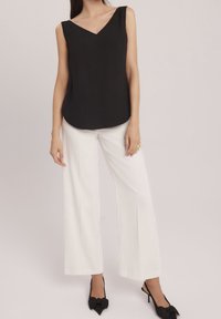 Top negro sin mangas con escote en V, combinado con pantalones anchos blancos. El conjunto cuenta con un tejido suave y una silueta relajada.