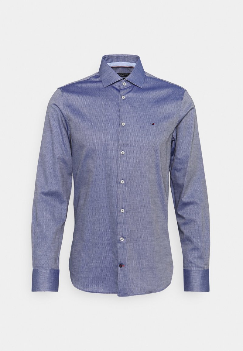 Camicia da uomo blu a maniche lunghe con bottone frontale, colletto a punta e piccolo logo sul lato sinistro del petto su sfondo bianco.