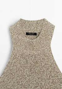 Beige gestrickter ärmelloser Pullover mit hohem Kragen. Texturiertes, dickes Garn mit einem subtilen melierten Muster. Das Etikett innen zeigt Marke und Herkunft.