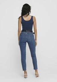 Navy tank top paired with high-waisted, fitted blue jeans featuring a frayed hem and a black belt adorned with studs.