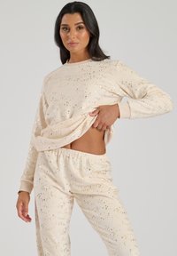 Completo loungewear beige composto da una maglia a maniche lunghe e pantaloni con vita elastica, entrambi decorati con motivi di stelle dorate su un tessuto morbido.