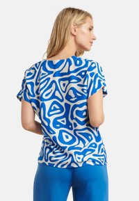Korte mouw top in blauw en crème, met een abstract patroon. Gemaakt van lichte stof met een ontspannen pasvorm en ronde halslijn.