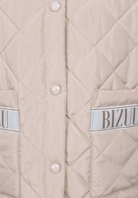 Beige gewatteerde jas met elastische zakken met "BIZUU" branding, drukknopen en een gladde, glanzende stoftextuur.