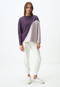 Felpa color block viola e grigia con scollatura rotonda e maniche lunghe, abbinata a joggers bianchi a gamba affusolata e sneaker bianche.