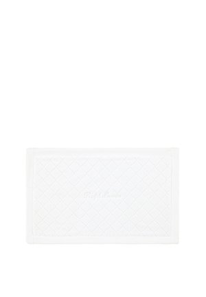 Tapis de bain rectangulaire blanc matelassé à motif losange et broderie subtile au centre, posé sur un fond blanc uni.