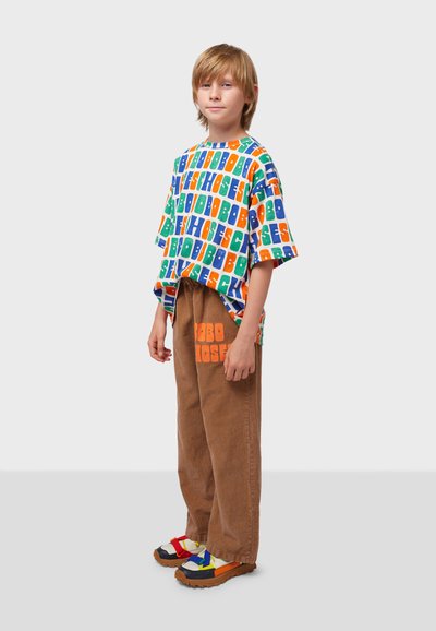 Short-sleeve, multicolored graphic t-shirt with letters, brown corduroy pants with orange print, and colorful chunky sandals.