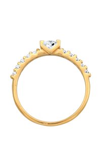Anello d'oro con una pietra centrale a forma di cuore, circondata da piccole pietre trasparenti lungo la fascia, finitura liscia e superficie lucidata.