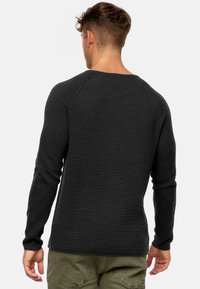 Sort langærmet sweater med ribbet tekstur, rund halsudskæring og raglanærmer, parret med olivengrønne bukser.