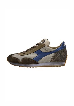 Zapatilla con parte superior de lienzo beige, acentos de cuero azul y detalles de ante marrón. Presenta cordones marrones y una suela de goma.