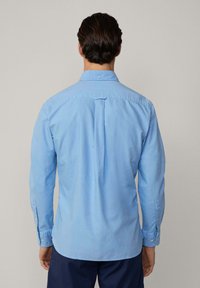 Light blue button-up shirt made from cotton. Features a back yoke, long sleeves, button cuffs, and a curved hemline. No visible patterns.