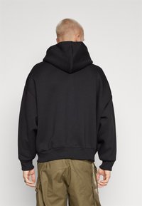 Black hooded sweatshirt with a loose fit, ribbed cuffs and hem, soft texture, no visible patterns or logos. Displaying the back view.