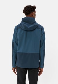 Giacca impermeabile di colore blu scuro con cappuccio aderente, schiena ventilata e design a blocchi di colore; presenta una texture liscia e opaca.