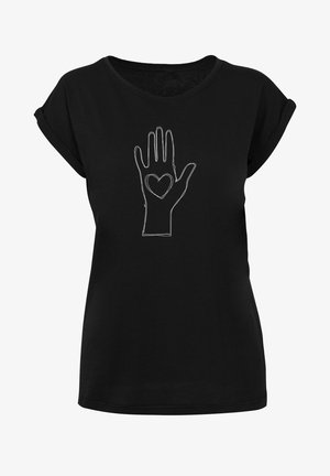 T-shirt noir à manches courtes avec un dessin en ligne blanche d'une main avec un cœur sur la paume, associé à un pantalon blanc ajusté et des baskets.
