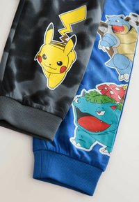 Juodos ir mėlynos sportinės kelnes su grafikos atspaudu Pikachu, Blastoise ir Bulbasaur. Su raukšlėtomis rankovėmis ir lygiu audinio paviršiumi.