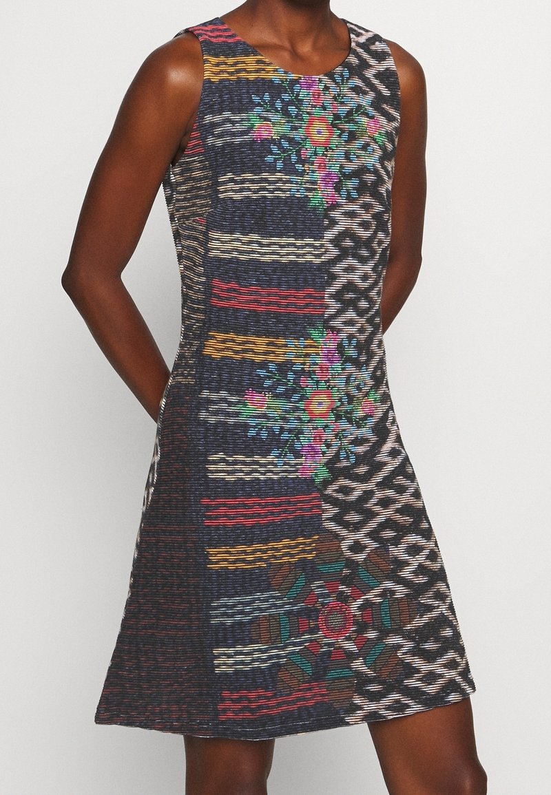 Robe sans manches avec motifs mélangés comprenant des rayures colorées, des motifs floraux et des imprimés géométriques sur un fond sombre.