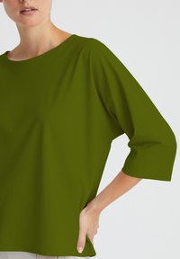 Olivgrüne, locker sitzende Bluse mit weitem Ausschnitt und Dreiviertelärmeln. Weiche Textur mit subtilem Fall, konzipiert für Komfort.