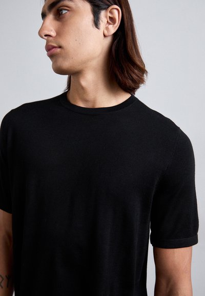 Schwarzes T-Shirt mit kurzen Ärmeln und Rundhalsausschnitt, aus einem glatten Stoff gefertigt. Mit feinem Rippmuster am Halsauschnitt und den Ärmelkanten.