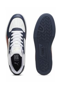 Zapatillas con una parte superior de cuero blanco, acentos en azul marino y rojo, diseño con cordones, puntera perforada y suela de goma texturizada con patrón.