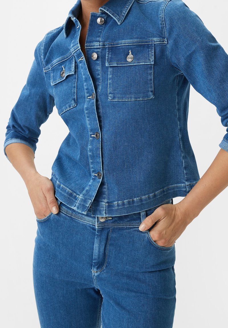 Blå denimjacka med krage, två framfickor, silverfärgade knappar och en kortad passform. Ytan är slät med lätt blekning.