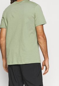 Camiseta de algodón verde claro con cuello redondo y mangas cortas, que presenta un ajuste relajado y una textura suave y uniforme.