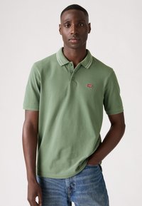 Green polo shirt with white accent stripes on the collar, made of soft fabric, featuring a small red Levi's logo on the chest.