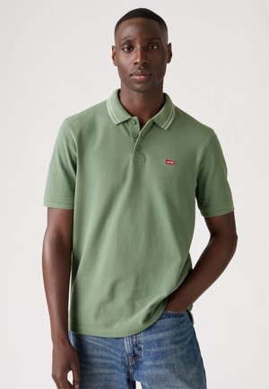 Green polo shirt with white accent stripes on the collar, made of soft fabric, featuring a small red Levi's logo on the chest.