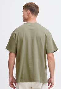 T-shirt verde oliva a maniche corte con una vestibilità rilassata, scollo rotondo e dettagli di cucitura sobri. Materiale in cotone liscio, senza motivi visibili.