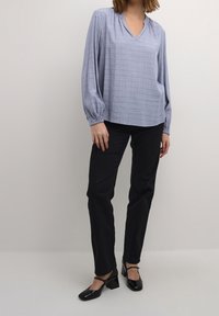 Blouse bleu clair à col en V avec manches longues resserrées, associée à un pantalon noir ajusté et des chaussures à talons blocs noires. Texture rayée subtile.