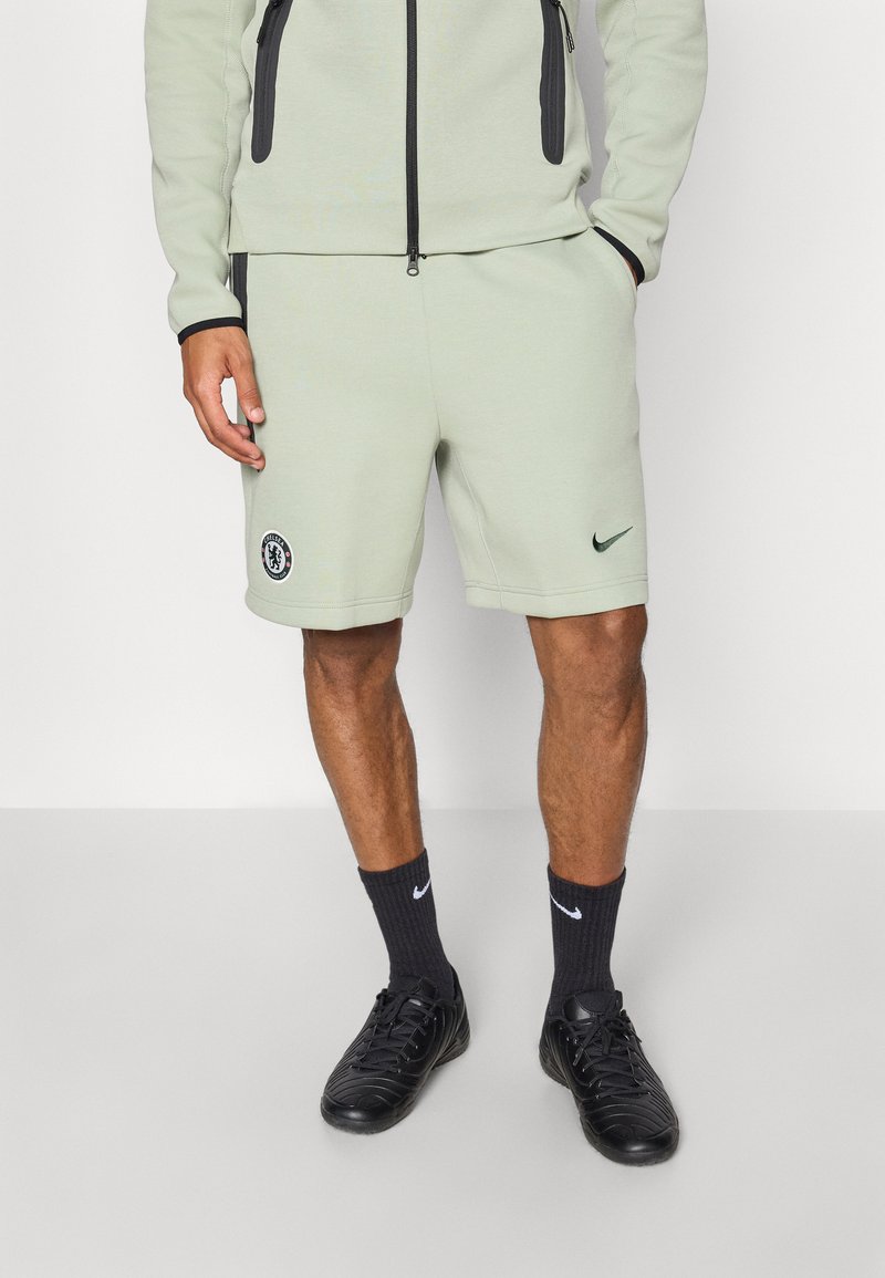 Világos zöld Nike sportnadrág, rugalmas derékkal, logóval és zsebekkel. Fekete sportcipővel és sötét zoknival párosítva.
