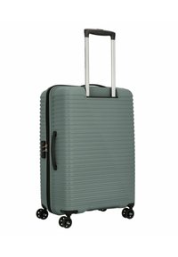 Valise rigide vert atténué avec des rainures verticales, poign handle télescopique et quatre roues noires pour la mobilité. Fermeture à glissière avec une poignée latérale.