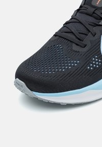Baskets de course noires avec une tige en mesh, ornées d'accents bleus, d'une semelle extérieure grise et d'un design texturé. Logo Nike sur le talon.