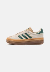 Sneakers Adidas Gazelle z kremowym welurowym wierzchem, zielonymi paskami i jasnobrązową gumową podeszwą, z teksturowanym noskiem i subtelnym logo.
