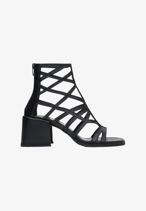 Black high-heeled sandal with a strappy design, featuring a block heel and zip closure at the back. Made from leather with a smooth texture.