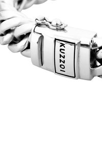 Silverkedjearmband med stora sammanlänkade länkar och ett rektangulärt spänne med en logotyp. Slät metallisk yta med polerad textur.