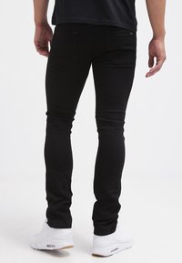 Jeans negros ajustados con una textura suave, que presentan dos bolsillos traseros y una etiqueta de marca sutil. Combinados con zapatillas deportivas blancas.
