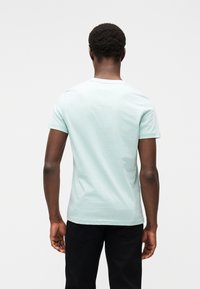 Ανοιχτό πράσινο βαμβακερό μπλουζάκι με κοντά μανίκια, στρογγυλή λαιμόκοψη και λεία υφή, σχεδιασμένο με απλό, μίνιμαλ στυλ.