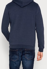Felpa blu navy realizzata in materiale morbido, con tasca a marsupio e polsini a coste, abbinata a jeans in denim scuro con tasche posteriori.