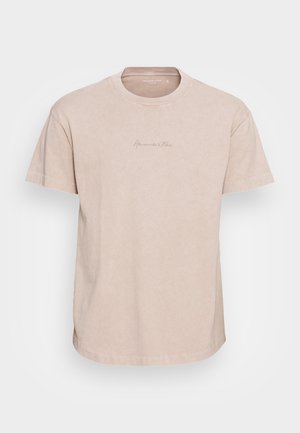 T-shirt in cotone beige con collo rotondo, maniche corte e un logo stampato sottile sul petto. Tessuto morbido e leggermente testurizzato.