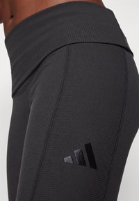 Μαύρες ριγέ κολάν με ψηλή μέση και υφή, διακοσμημένα με ένα γυαλιστερό μαύρο λογότυπο στο κάτω αριστερό μέρος.