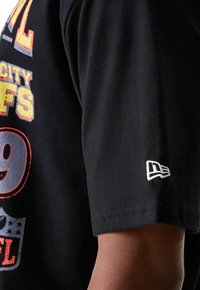 T-shirt en coton noir avec imprimé graphique coloré représentant le texte "NFL City 9." Comprend un petit logo blanc sur la manche. Design à manches courtes.