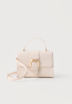 Beige strukturierte Handtasche mit obere Trageschlaufe, abnehmbarem Schulterriemen und goldfarbenem, gebogenem Schnappverschluss vor hellem Hintergrund.