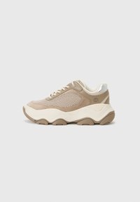 Sneaker beige con materiali in rete e suede, forma arrotondata, dettagli testurizzati, lacci tonali e una suola spessa e ondulata.