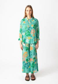 Bloemenprint set met een lichtgroene blouse met oranje, blauwe en roze bloemen, en brede bijpassende broek. Zachte stofstructuur.