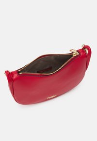 Sac bandoulière en cuir rouge avec un design arrondi, fermeture éclair dorée et poche intérieure. Présente un logo doré à l'avant.