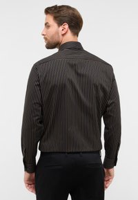 Camicia nera a maniche lunghe con strisce verticali strette arancioni. Presenta un colletto classico e polsini con bottone.