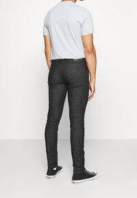 Jeans negros ajustados con una textura suave, diseño de cinco bolsillos y detalles de costura sutiles, combinados con una camiseta gris de manga corta y zapatillas negras.
