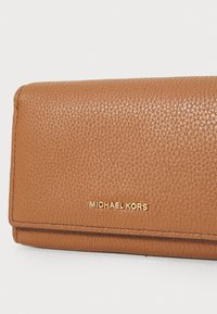 Portafoglio in pelle marrone con superficie texturizzata, dotato di un logo dorato "MICHAEL KORS". Design compatto e rettangolare con cuciture visibili.