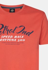 Červené bavlněné tričko s kulatým výstřihem, krátkými rukávy a potiskem v námořnické modři: "Petrol Ind SPEED RACE DAYTONA 500."