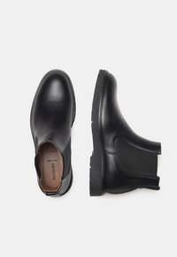 Stivali alla caviglia in pelle nera con pannelli laterali elasticizzati, design a punta rotonda, suole in gomma testurizzata e dettagli di cucitura discreti.